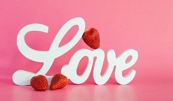 Der weiße Schriftzug Love vor rosa Hintergrund, dekoriert mit Erdbeeren